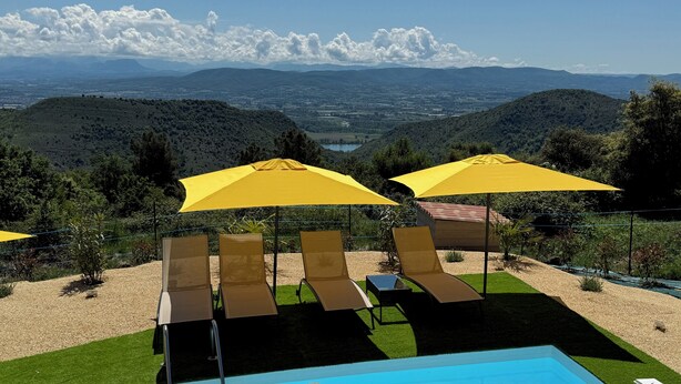 Zona de piscina con sillones reclinables y sombrillas amarillas, con vistas a un paisaje pintoresco con montañas y un valle.