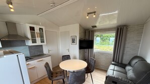 Una cocina moderna con refrigerador, estufa y armarios. Hay una mesa de comedor con cuatro sillas y un sofá. Un televisor está montado en la pared.