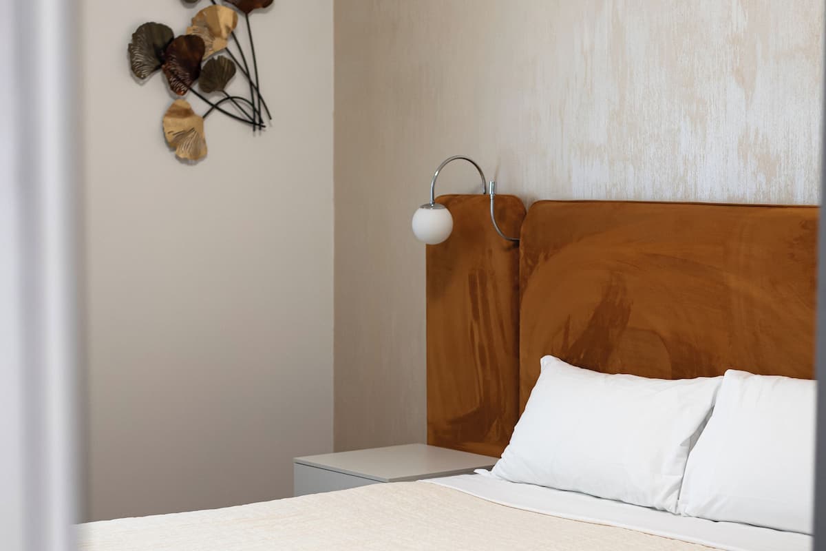 A neatly made bed with white linens, a wooden headboard, and a bedside table with a lamp.