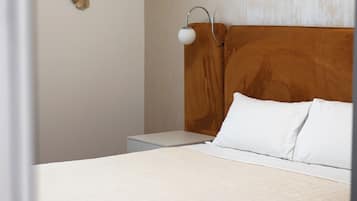 A neatly made bed with white linens, a wooden headboard, and a bedside table with a lamp.