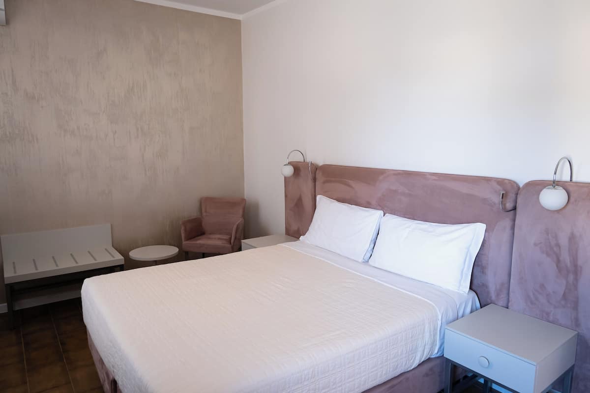A neatly arranged hotel room with a large bed, a small round table, a chair, and a nightstand with a drawer.