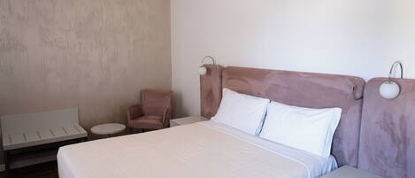 A neatly arranged hotel room with a large bed, a small round table, a chair, and a nightstand with a drawer.