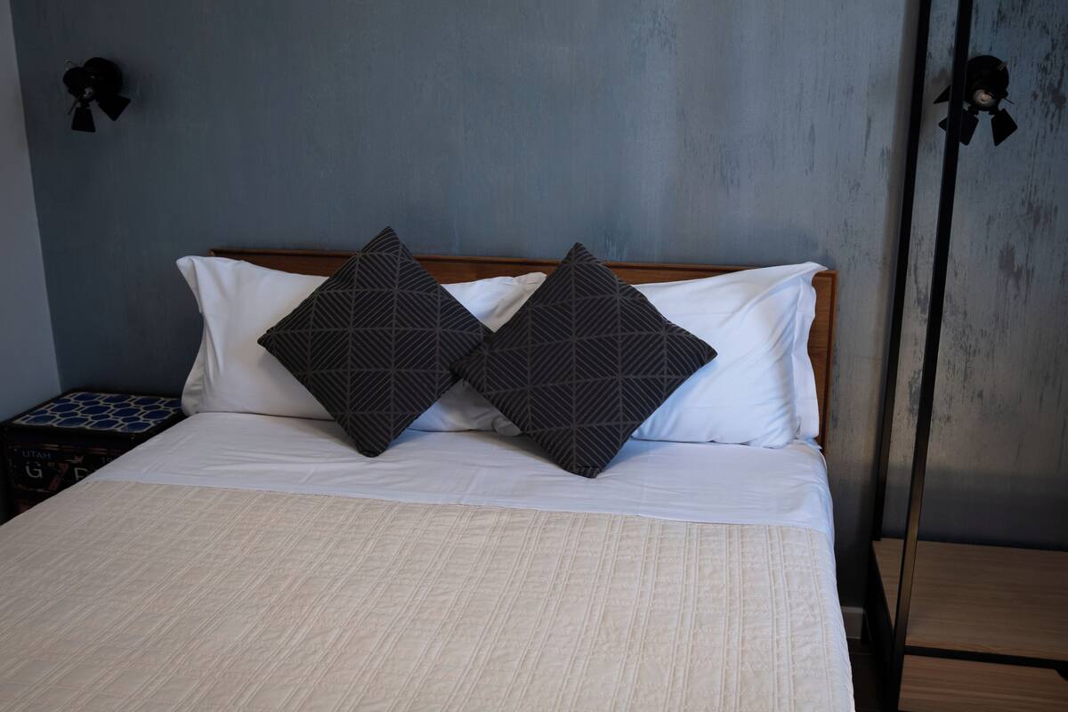 A neatly made bed with a white duvet, two dark patterned pillows, and a wooden headboard.