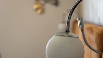 A close-up of a modern bedside lamp with a metallic base and a white lampshade, positioned next to a bed with white bedding.