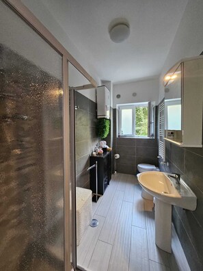 Un bagno moderno con box doccia in vetro, lavandino bianco e parete rivestita di piastrelle scure.
