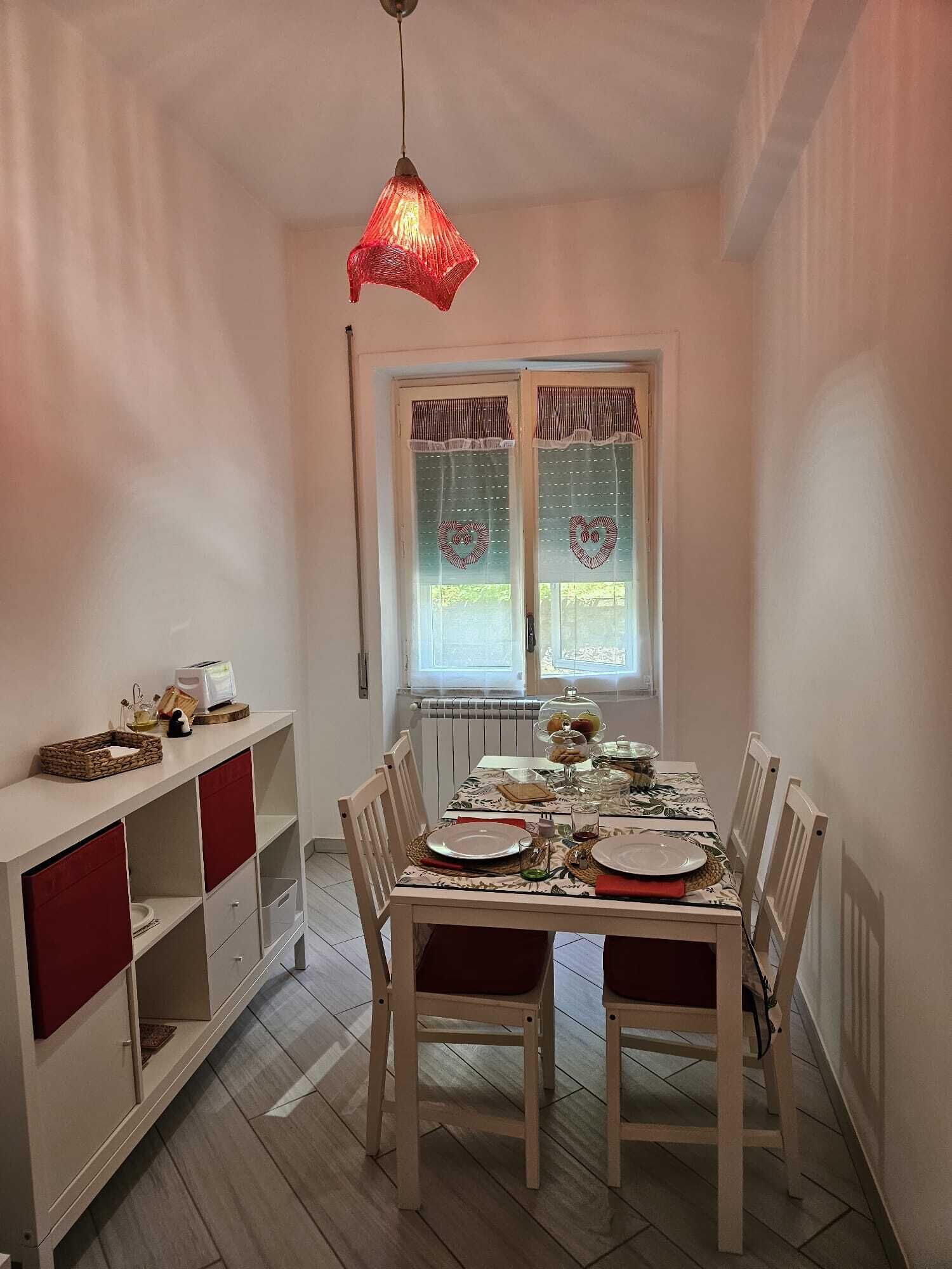 Un comedor con una mesa preparada para dos, un armario blanco con puertas rojas y una lámpara colgante roja.