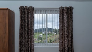 Quarto com janela que oferece vista para uma paisagem acidentada e edifícios.