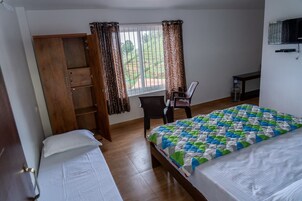 A bedroom with a bed, a wooden wardrobe, a desk with a chair, and a window with curtains.
