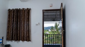 Quarto com cortina, dispensador de água e vista para uma paisagem verde através de uma porta aberta.