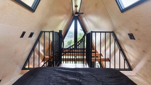 A room with a sloped ceiling, a bed, a staircase, and a view through a skylight. - Designer A-Frame Treehouse with hot tub on river (Johnson)