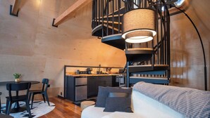 A modern interior with a spiral staircase, a cozy sofa, a dining table with chairs, and a kitchen area. - Designer A-Frame Treehouse with hot tub on river (Johnson)
