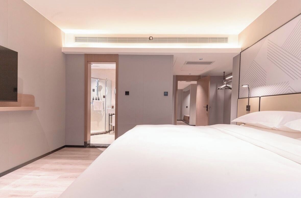 Una habitación de hotel moderna con una cama grande, una mesita de noche, un espejo y un vestidor.