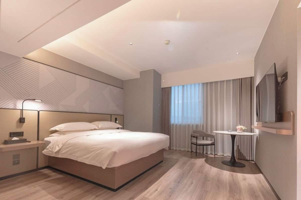 Ett modernt hotellrum med en stor säng, ett sängbord, en lampa och ett litet runt bord med en stol.