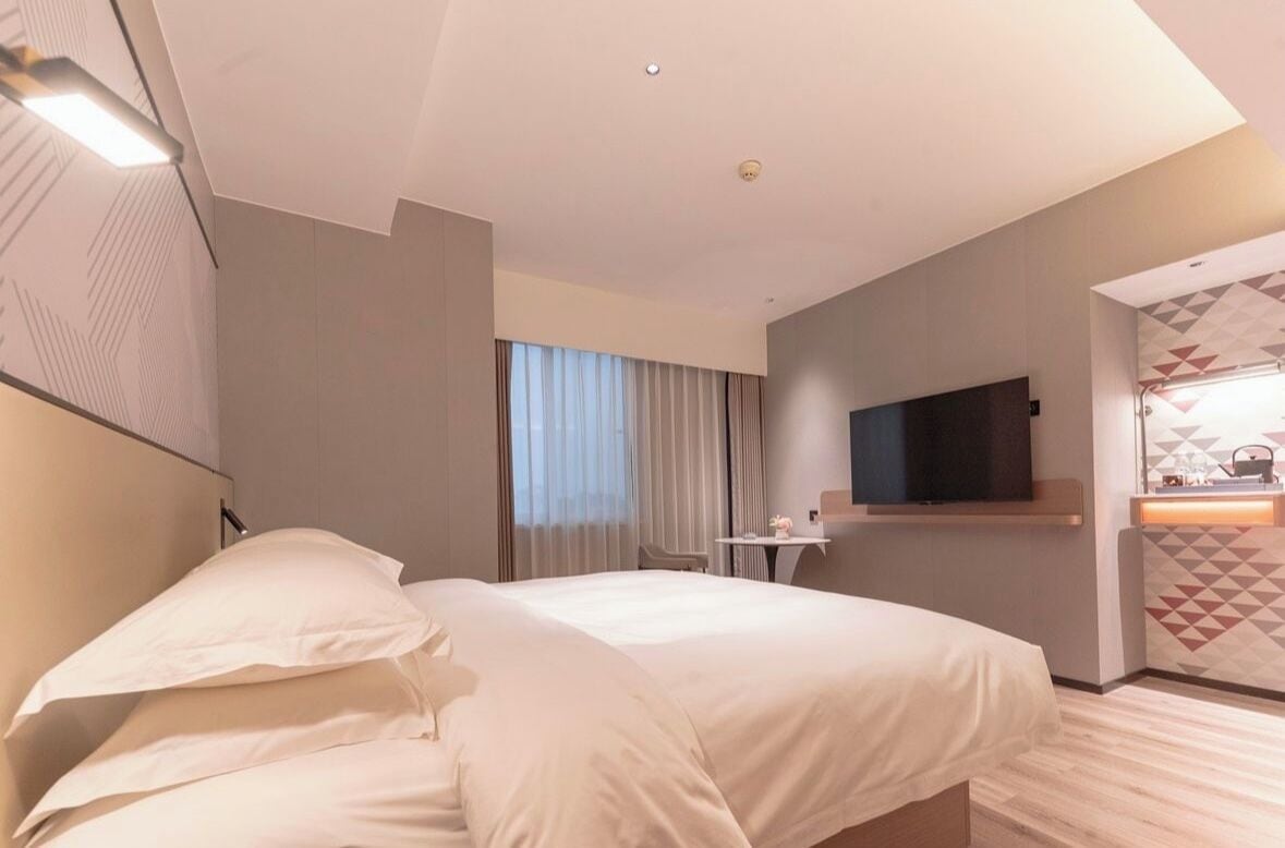 Una habitación de hotel con una cama grande, un escritorio, un televisor y una ventana con cortinas.