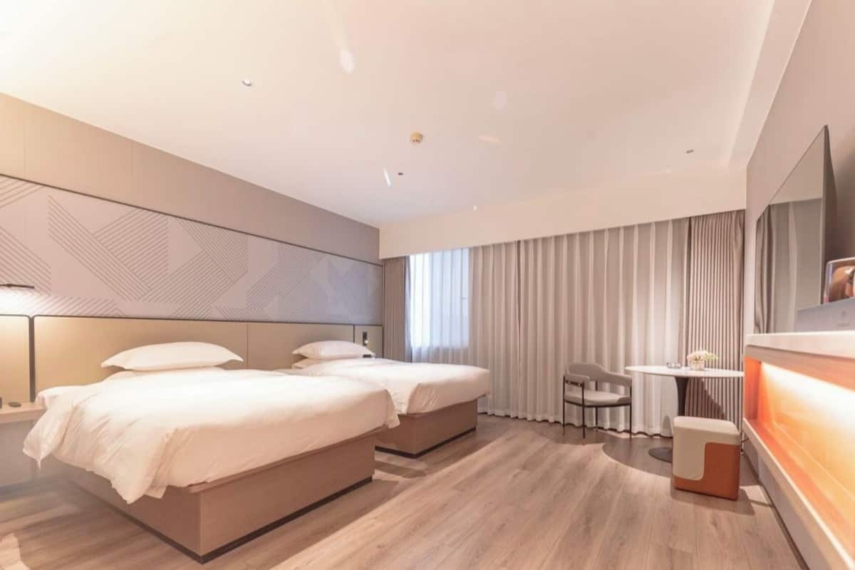 Ett modernt hotellrum med två sängar, ett skrivbord och en sittgrupp.