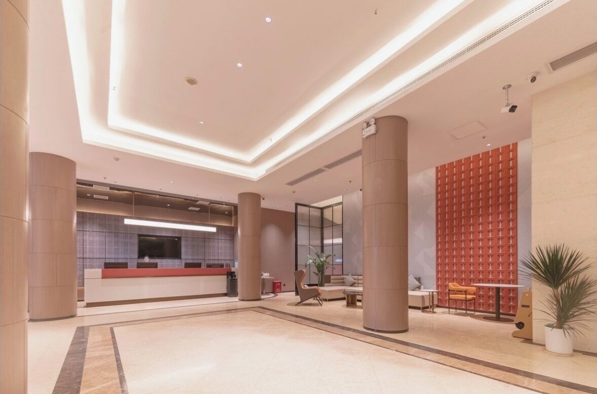 Een ruime lobby met een receptiebalie, een zithoek en een rode, geruite wand.