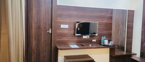 A hotel room with a wooden wardrobe, a television, a small table, and a bench.