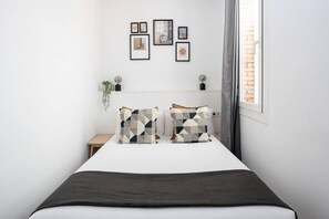 A neatly arranged bedroom with a bed, a bedside table, a small plant, and a window with curtains.