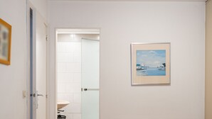 Ein Badezimmer mit einem weißen Waschbecken, einem gerahmten Meeresblick-Gemälde und einer Tür, die in einen anderen Raum führt.