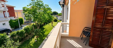 A residential balcony with a view of a green lawn and neighboring houses.