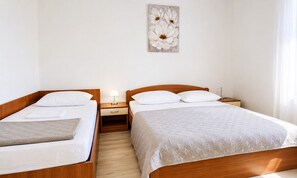 A hotel room with two single beds, a wooden headboard, a bedside table with a lamp, and a wall-mounted artwork.