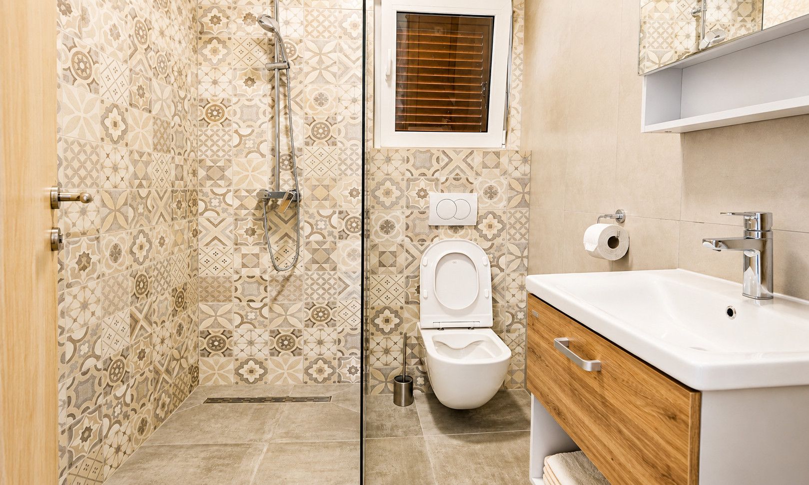 Een badkamer met patroon betegelde vloer, een douche, toilet en een wastafel met houten kastje.