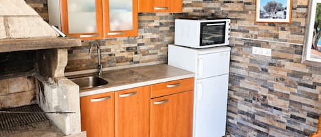 A compact kitchen with a stone backsplash, wooden cabinets, a built-in oven, and a microwave.