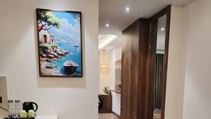 Une chambre d’hôtel moderne avec un plancher en bois, un bureau avec une chaise, un tableau représentant un paysage côtier et une armoire.