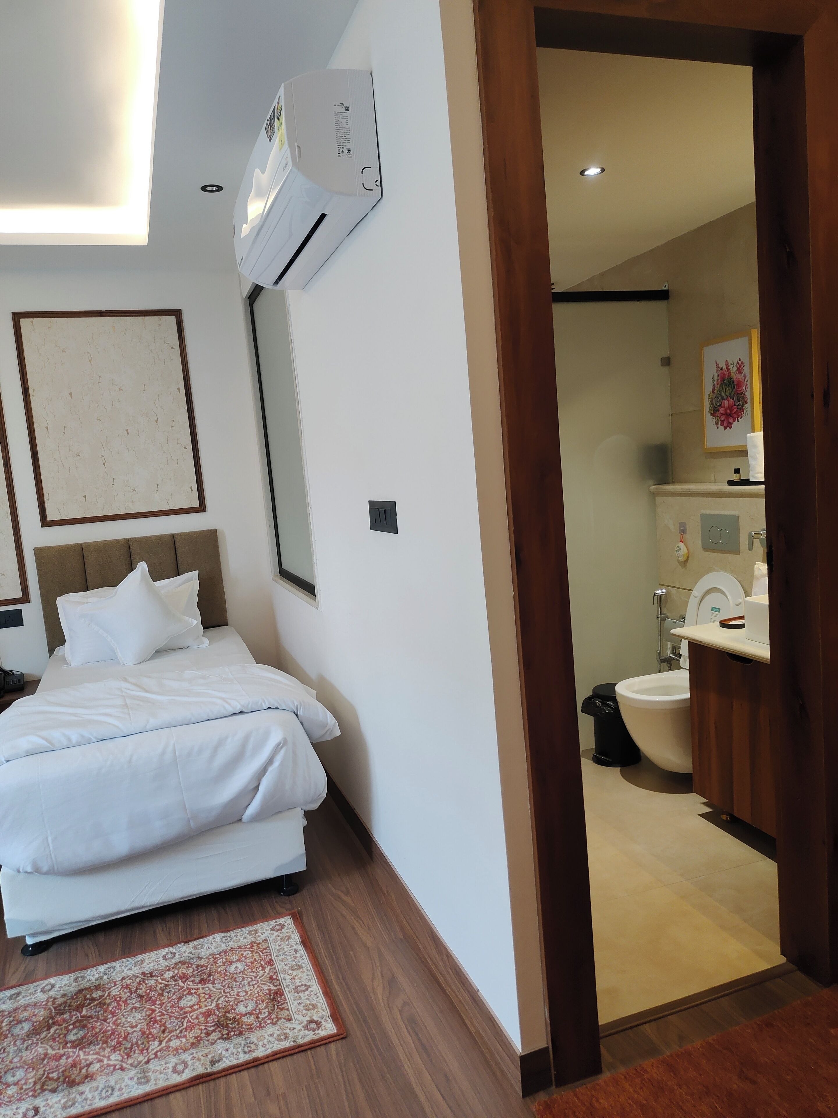 Ein Hotelzimmer mit Bett, Nachttisch, Klimaanlage, einem gerahmten Bild an der Wand und Blick ins Bad.