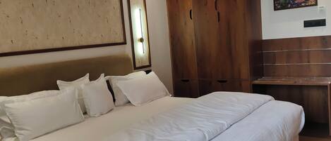 A neatly made bed with white linens, a wooden wardrobe, and a painting of hot air balloons on the wall.