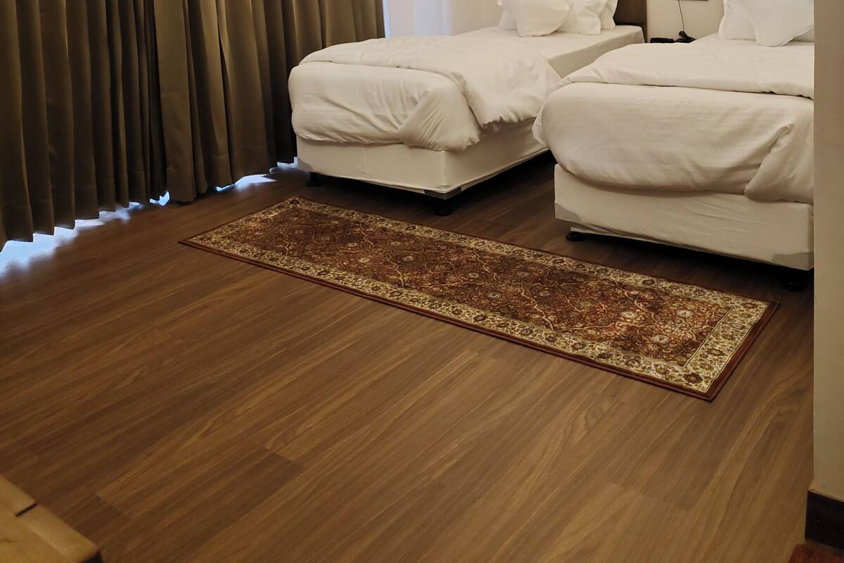 A hotel room with two beds, a ceiling fan, a large window with curtains, and a patterned rug.