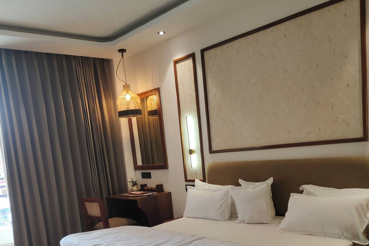 A large bed with white linens, a wooden headboard, a bedside table with a lamp, and a large mirror on the wall.
