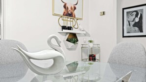 Una habitación moderna con una mesa de vidrio, sillas con forma de cisne blanco, una obra de arte enmarcada de una cabeza de toro y un estante con tazas negras y una pequeña planta.