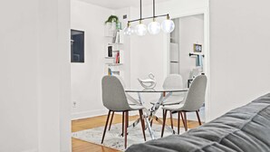 Un comedor moderno con una mesa de vidrio y sillas grises, una pared blanca y una lámpara colgante.