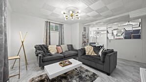 Een moderne woonkamer met een wit plafond, grijze banken, een witte salontafel en een zwarte vachttapijt.