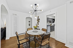 A dining area with a round table, chairs, a chandelier, and a kitchen in the background. - 4 Spacious Units | Near Downtown & Expo Center! (Louisville)