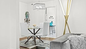 Et moderne spiseområde med et hvidt bord og stole, en hængende lampe samt kig til køkkenet.