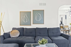 A modern living room with a grey sofa, a glass coffee table with a white vase, and abstract art on the wall. - 4 Spacious Units | Near Downtown & Expo Center! (Louisville)