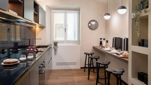 A modern kitchen with a central island, bar stools, and a window with blinds. - Arts & Crafts Apartments (Florence)