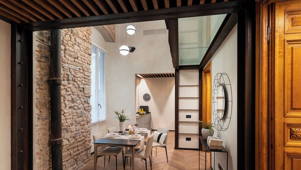A dining area with a stone wall, wooden beams, a table set for four, and a modern light fixture. - Arts & Crafts Apartments (Florence)