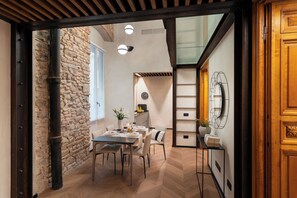 A dining area with a stone wall, wooden beams, a table set for four, and a modern light fixture. - Arts & Crafts Apartments (Florence)