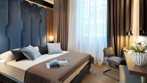 A modern hotel room with a large bed, a desk, and a chair. There is a window with curtains and a view of the city. - Arts & Crafts Apartments (Florence)