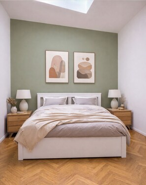 Un dormitorio con cama, dos mesitas de noche, una pared con arte abstracto y un tragaluz.