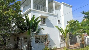 Un edificio de dos pisos con balcón, rodeado de exuberante vegetación y un jardín cuidado.