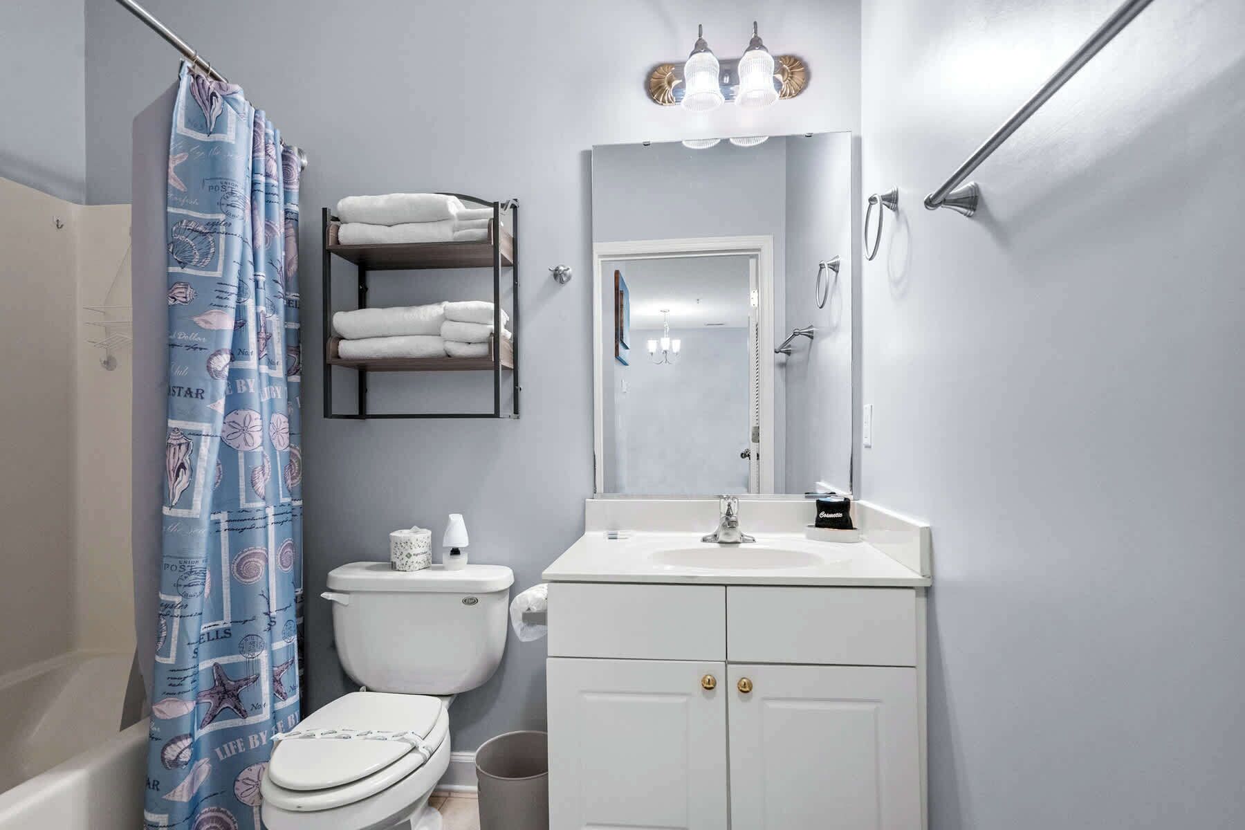 Une salle de bain avec des toilettes, un lavabo et un miroir. Il y a un porte-serviettes au-dessus des toilettes et un rideau de douche à motifs.