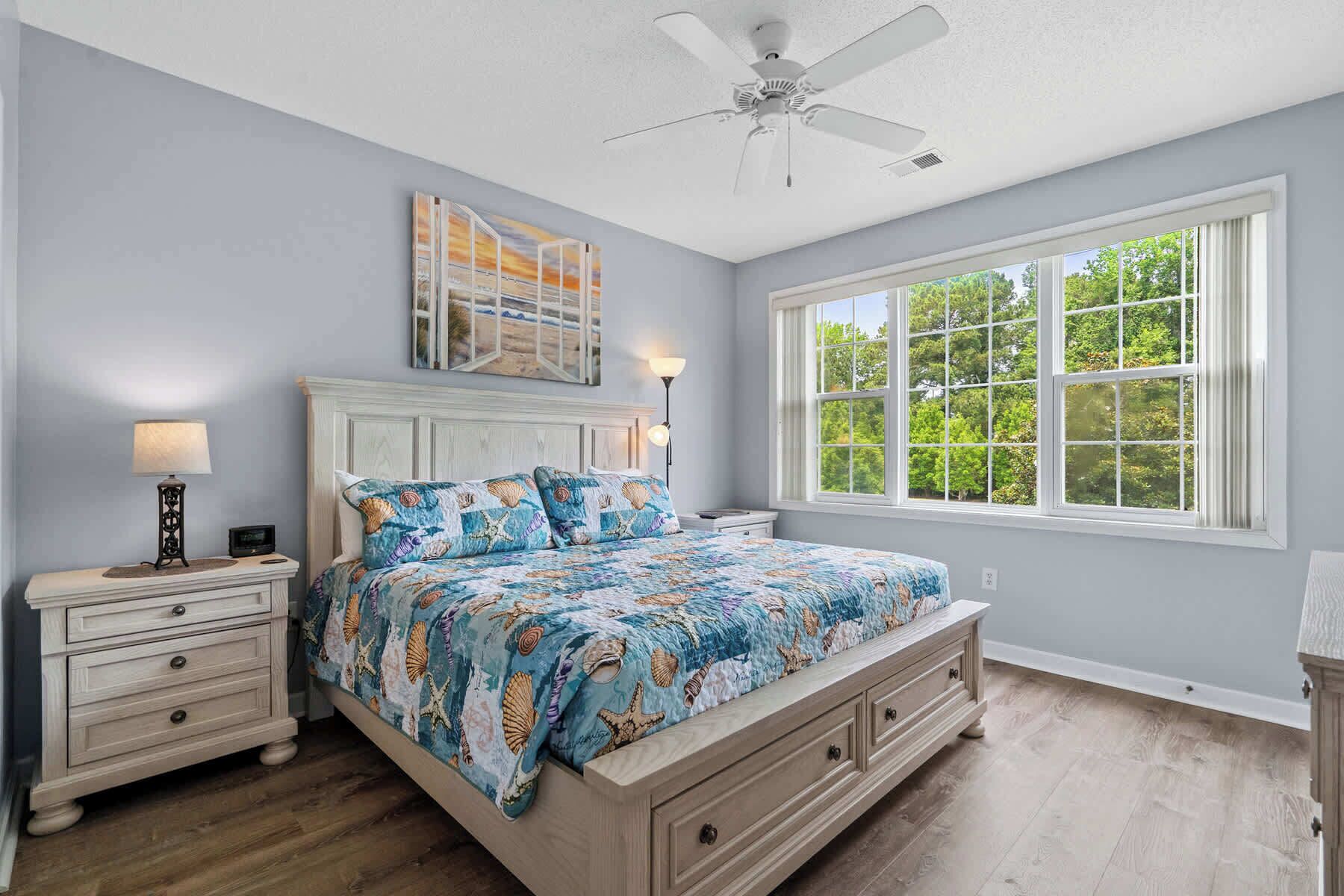 A bedroom with a bed, nightstands, a ceiling fan, and a large window.