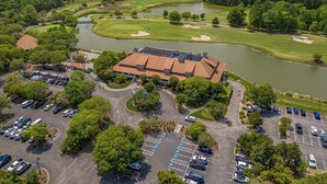 An aerial view of a golf course with a clubhouse, parking lot, and a lake. - River Crossing Unit 324 (North Myrtle Beach)