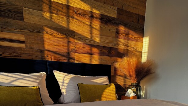 A bed with a white sheet, a dark headboard, and multiple pillows in various colors. - Zinna Monastery Post Office (Jüterbog)