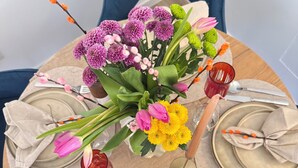 A round dining table set for four with a floral centerpiece, a red glass, and a glass of yellow liquid. - Zinna Monastery Post Office (Jüterbog)