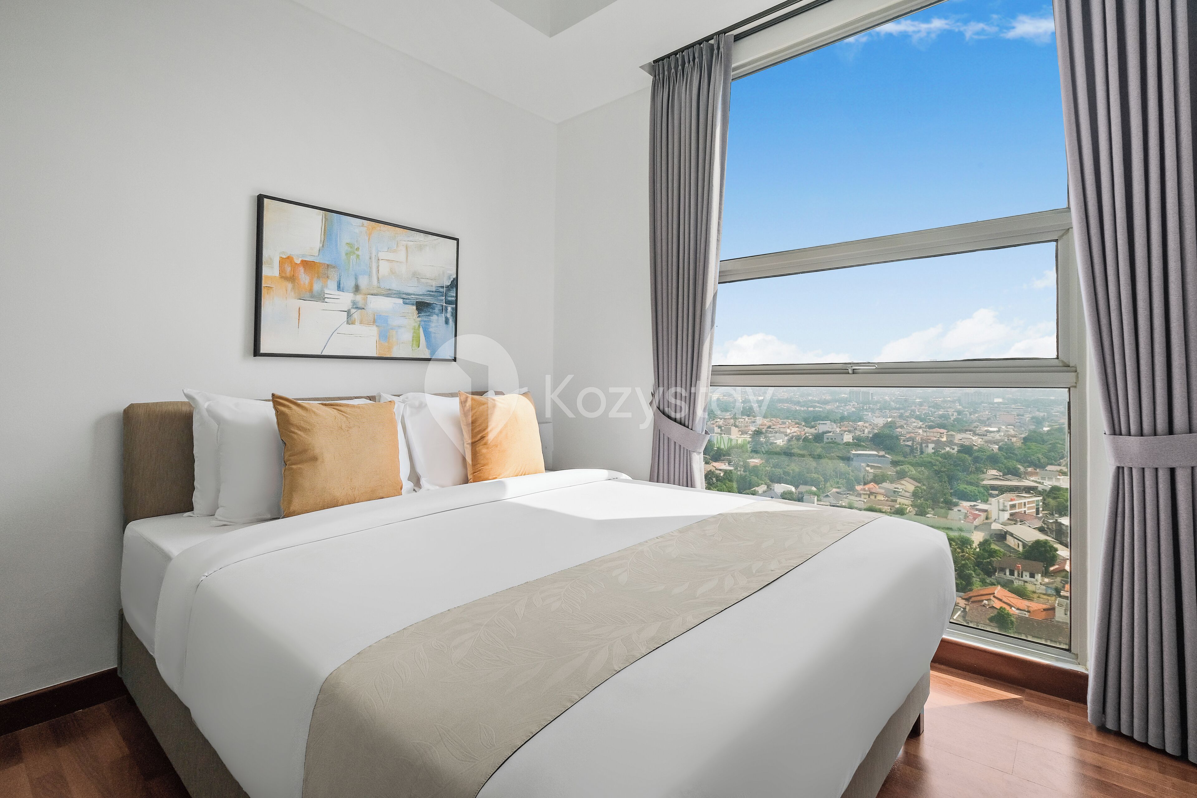 A hotel room with a large bed, a city view, and a painting on the wall.